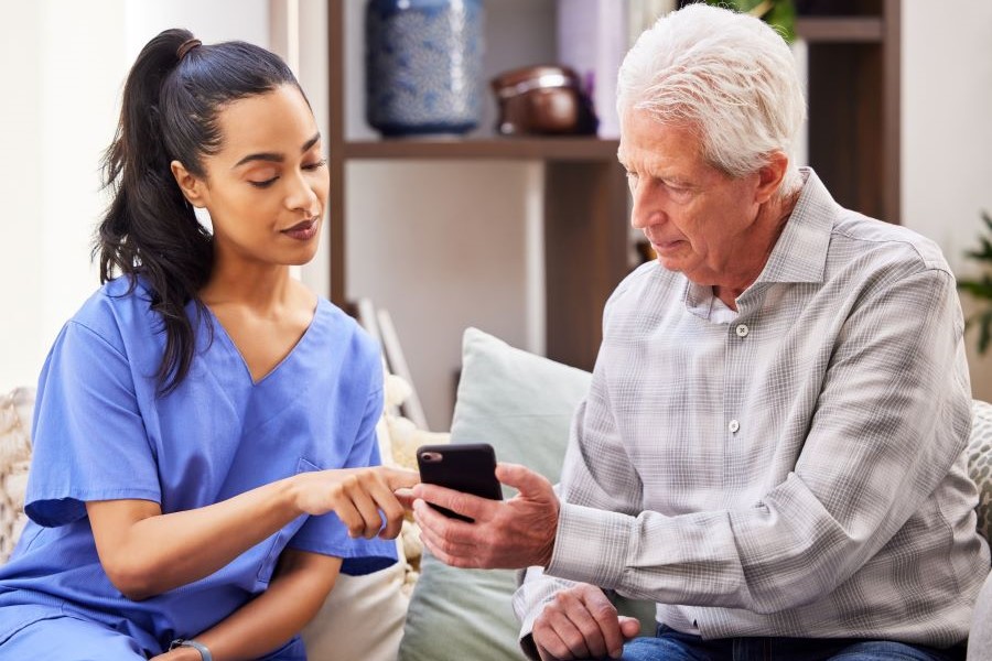 &Auml;lterer Mann l&auml;sst sich am Handy etwas von einer weiblichen Pflegekraft zeigen 