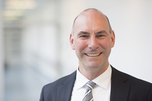 Portrait eines freundlich lächelnden Mannes mit grau gestreifter Krawatte. 
