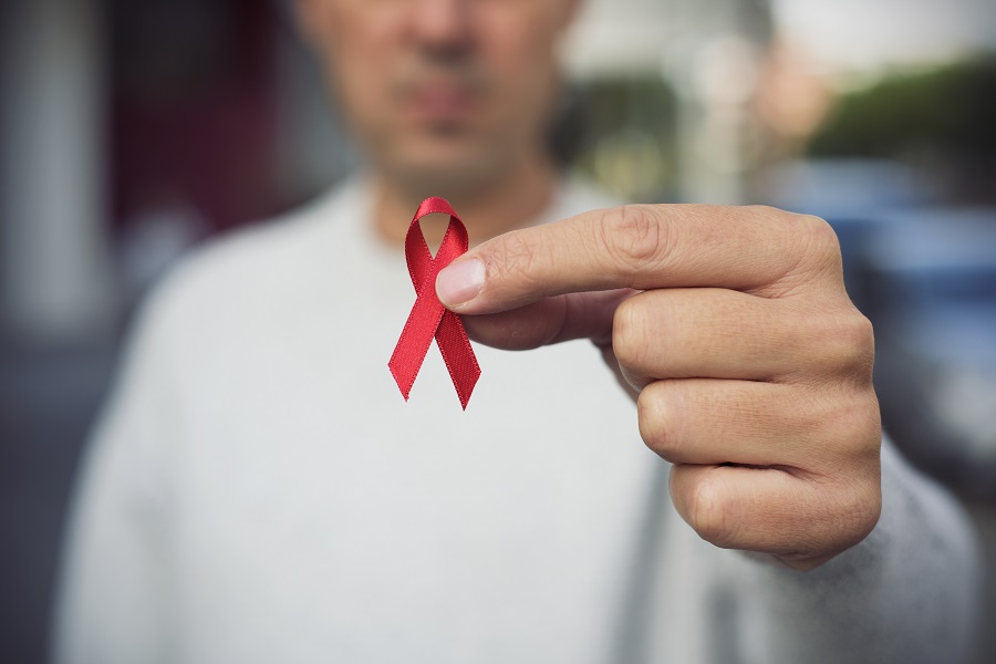 Junger Mann hält rotes Aids-Schleifchen in die Kamera