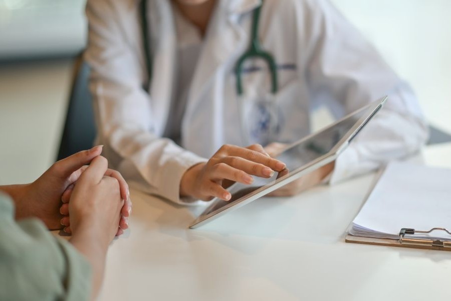 Eine Ärztin in weißem Kittel berät eine Patientin und zeigt ihr Informationen auf einem Tablet-Computer. Eine Ärztin in weißem Kittel berät eine Patientin und zeigt ihr Informationen auf einem Tablet-Computer.