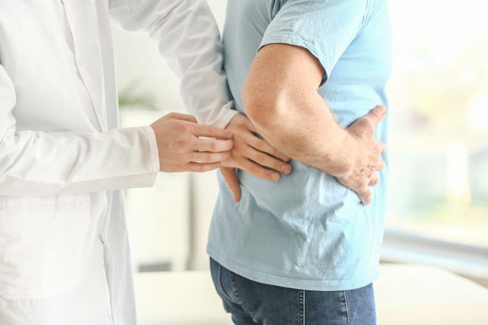 Ein Arzt klopft die Nierenregion eines Patienten bei einer Untersuchung ab.