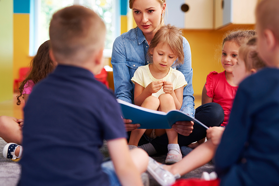Eine Erzieherin sitzt mit mehreren Kindern auf dem Boden und liest ihnen etwas vor. Eine Erzieherin sitzt mit mehreren Kindern auf dem Boden und liest ihnen etwas vor.