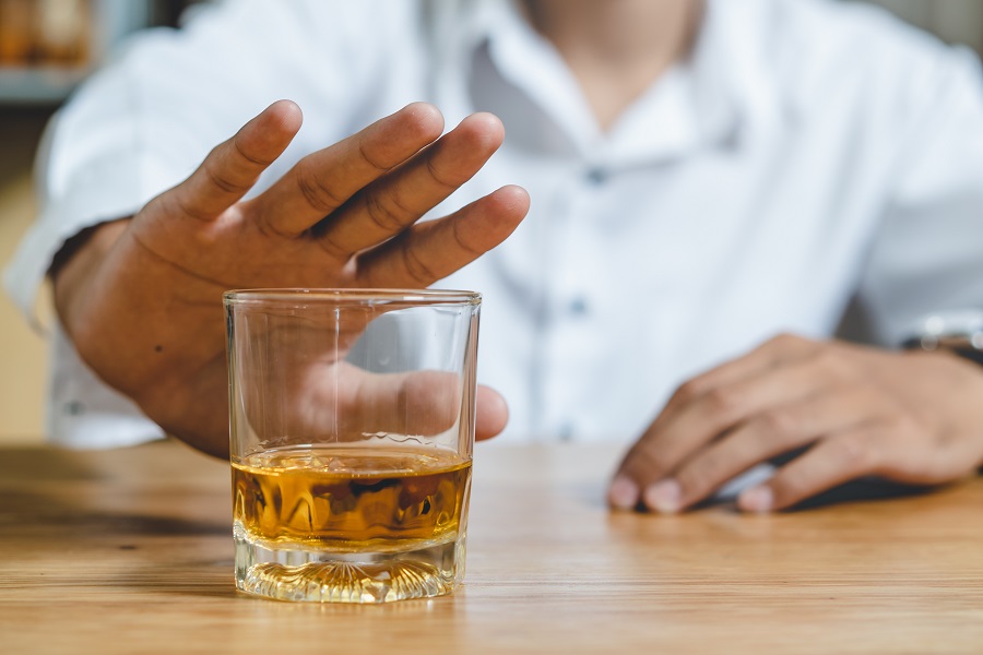 Ein Mann sitzt an einem Tisch und schiebt ein mit einer braunen Flüssigkeit gefülltes Glas von sich weg