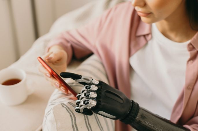 Eine Frau mit einer gesunden Hand und einer Prothesenhand schaut auf ihr Handy.