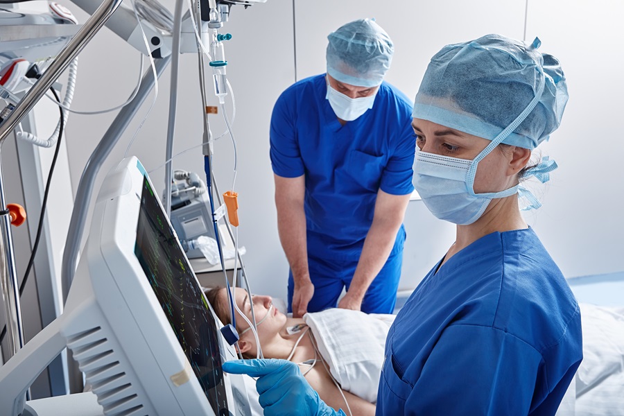  Krankenpflegerin und Krankenpfleger in OP-Kleidung betreuen Patientin auf der Intensivstation