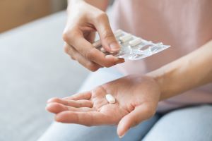 Auf einer Handinnenfläche liegt eine weiße Tablette. Mit der anderen Hand wird eine Tabletten-Verpackung gehalten. Auf einer Handinnenfläche liegt eine weiße Tablette. Mit der anderen Hand wird eine Tabletten-Verpackung gehalten.