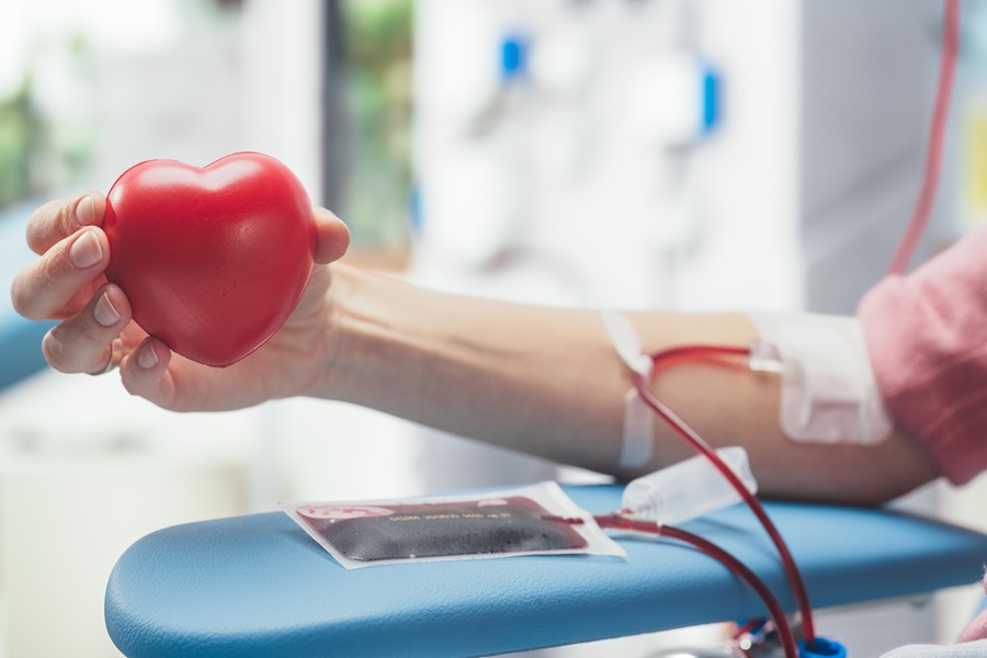 Nahaufnahme einer weiblichen Hand bei einer Blutspende, ein rotes Kunststoffherz haltend