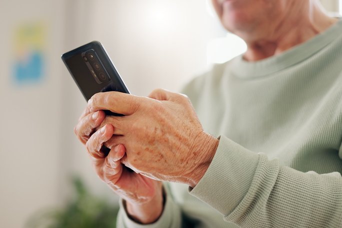Eine ältere Person hält ein Mobiltelefon in den Händen