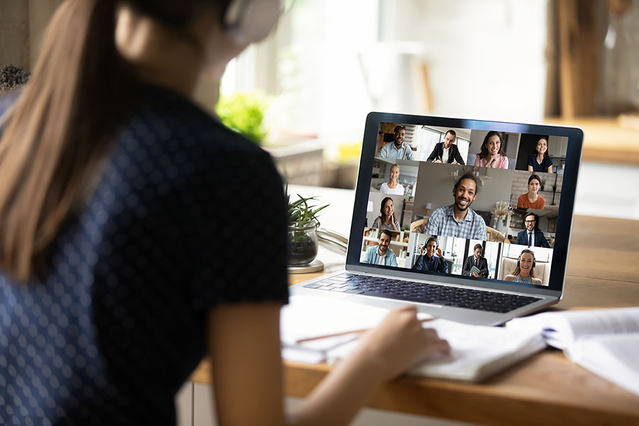 Junge Frau sitzt am Bildschirm und ist in einer Videokonferenz mit anderen Kolleginnen und Kollegen 