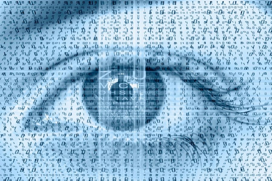 Bildausschnitt mit Foto eines offen blickenden Auges in dessen Pupille sich eine dunkle Gestalt spiegelt. Grafisch überlagert ist das Bild mit kleinen Zahlen und Buchstaben in regelmäßiger Anordnung sowie zentral durch die Iris verlaufenden senkrechten und waagerechten Bildstörungen.