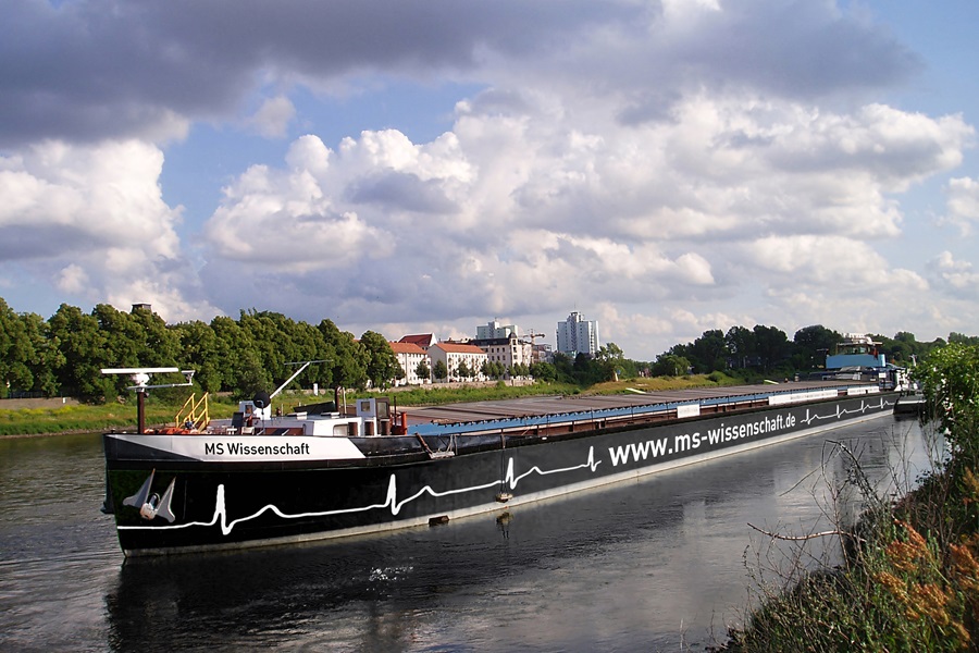 Das zu einem schwimmenden Ausstellungsraum umgebaute, ehemalige Binnenfrachtschiff „MS Wissenschaft“ auf einem Fluss.