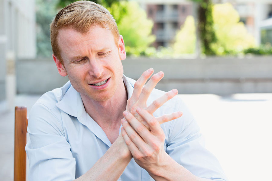 Mann umfasst sich mit schmerzerfüllten Gesichtsausdruck seine Hand.