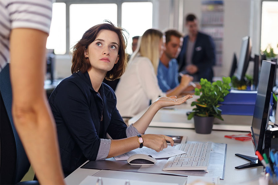 Frau mit fragendem Gesichtsausdruck in einem Gro&szlig;raumb&uuml;ro.