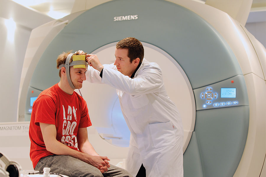 Robert Darkow, Mitarbeiter der Klinik für Neurologie mit Experimenteller Neurologie an der Charité, befestigt die Elektroden am Kopf eines gesunden Probanden. Während dieser im Tomografen Sprachübungen absolviert, misst Darkow den Einfluss der elektrischen Stimulation auf die Hirnaktivität.