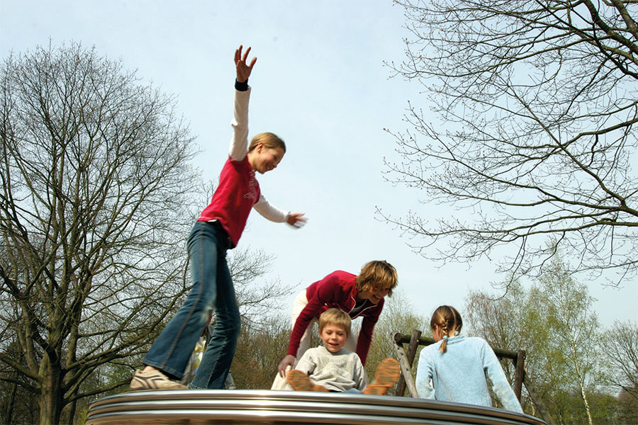 Kinder spielen mit Mutter auf einem Spielplatz in einem Park.