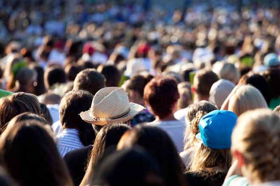 Blick auf eine dichte Menschenansammlung, es sind nur die Hinterköpfe zu sehen. Eine Person trägt einen beigen Hut, eine Person daneben eine blaue Mütze