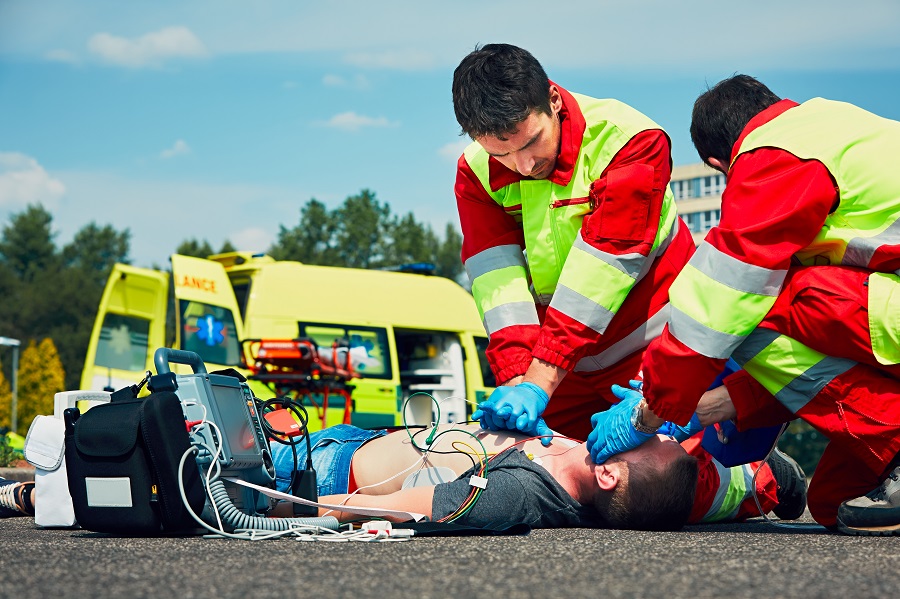 Zwei Rettungssanitäter behandeln einen jungen Mann, er auf der Straße liegt. 