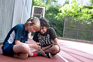 Zwei Jungen schauen auf Smartphone. Ein Junge trägt ein Hörgerät.