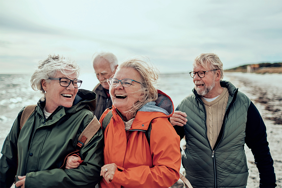 Zwei ältere Paare spazieren lachend am Strand Zwei ältere Paare spazieren lachend am Strand