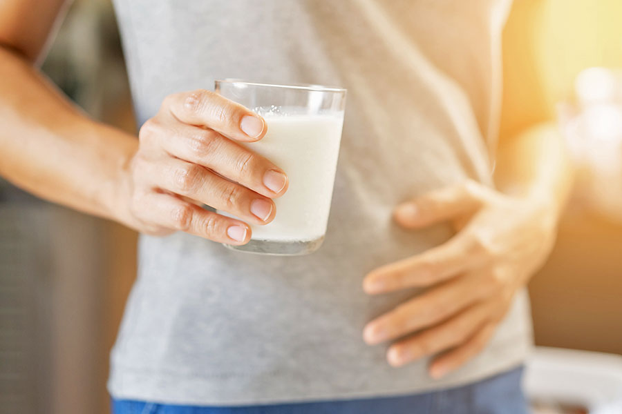 Frau mit Milchglas in der Hand hält sich den Bauch
