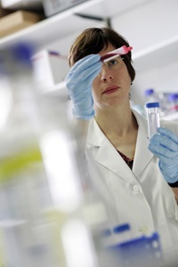 Eine Frau in einem Labar, sie hat Handschuhe an und h&auml;lt R&ouml;hrchen mit Blut und einer Fl&uuml;ssigkeit in ihren H&auml;nden