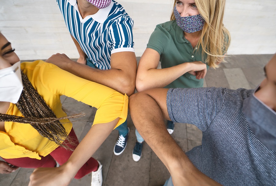 Junge Leute mit Gesichtsmasken begrüßen sich mit Ellbogen.