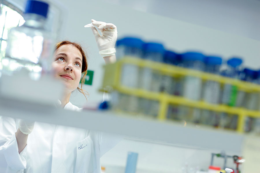 Junge Wissenschaftlerin hält im Labor ein Versuchsröhrchen gegen das Licht und kontrolliert dessen Inhalt. 