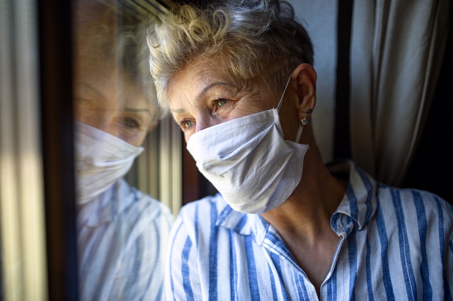 Frau mit Maske schaut aus dem Fenster