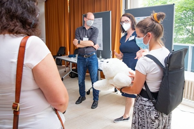 Eine Gruppe von Menschen betrachtet einen Roboter, der wie eine kleine Robbe aussieht. 