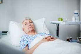 Ältere Patientin liegt im Krankenhausbett und schaut nachdenklich an die Decke.