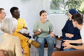 Sechs Personen verschiedenen Alters, Geschlechts und Herkunft sitzen auf Stühlen im Kreis und diskutieren angeregt.