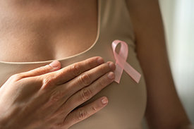 Nahaufnahme eines weiblichen Oberkörpers mit beigefarbenem Top und rosafarbener Schleife, die Aufmerksamkeit für Brustkrebs schaffen soll