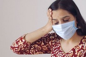 Frau mit Maske hält sich die Hand an den Kopf