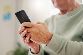 Eine ältere Person hält ein Mobiltelefon in den Händen