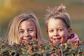 2 Kinder schauen hinter Gebüsch hervor