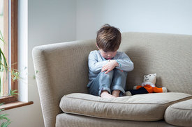 Ein kleiner Junge sitzt alleine in einer Sofaecke.