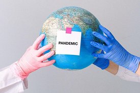 Drei Hände mit Gummihandschuhen halten eine Weltkugel mit einem Schild PANDEMIC