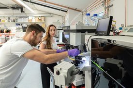 Ein junger Mann arbeitet an einem Massenspektrometer, seitlich steht eine junge Frau