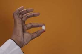 Eine Hand hält eine Tablette zwischen Daumen und Zeigefinger.