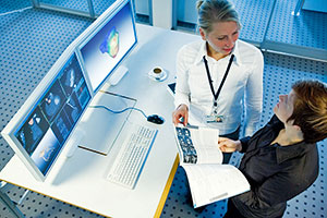 Zwei miteinander diskutierende Wissenschaftlerinnen stehen vor Monitoren mit CT- und MRT-Aufnahmen des Herzens.